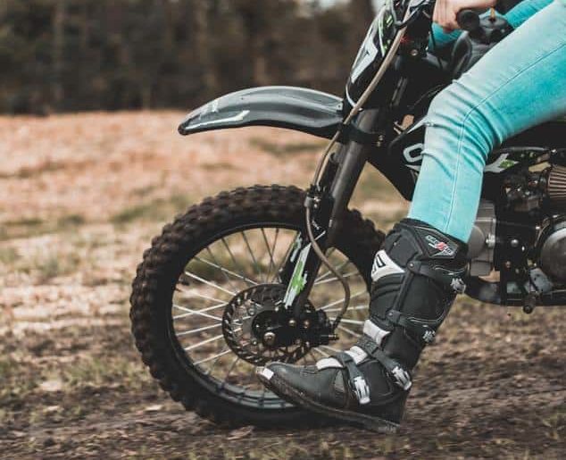 Dirt bike front tire with riders leg in front for balance.