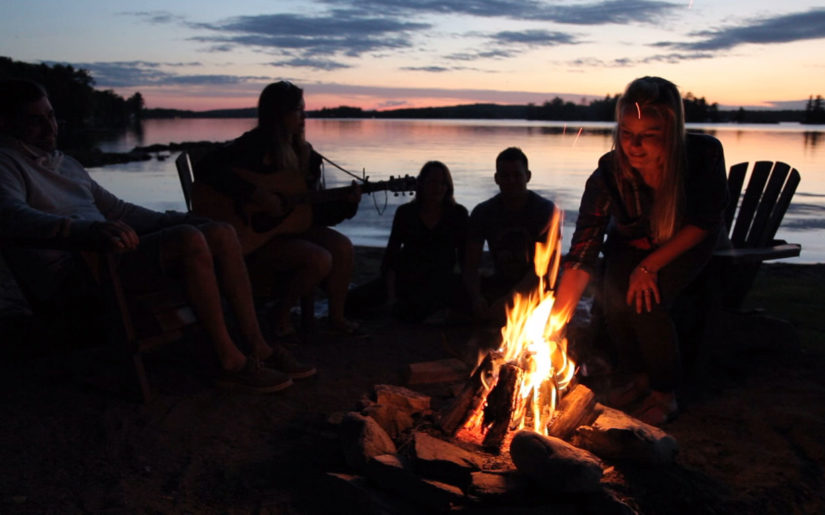 Cottagers sitting around campfire, singing songs.