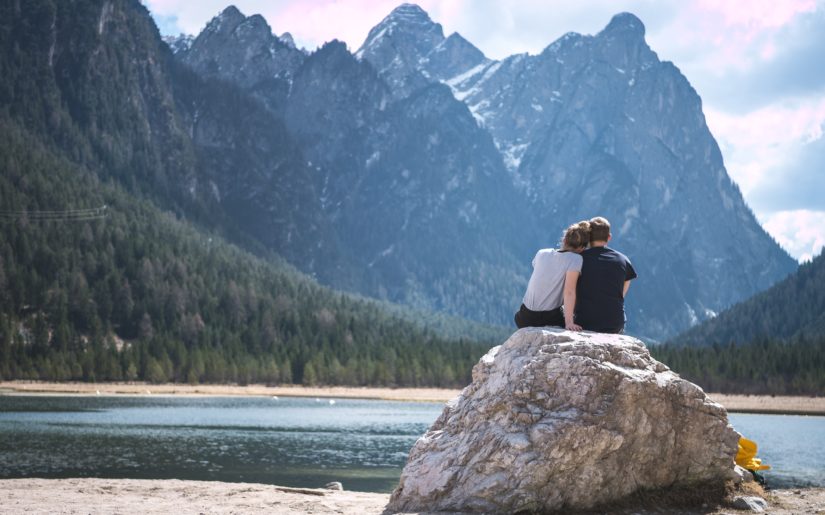 Couple sitting on a large rock, taking in the scenes from a lake, forest and mountains.
