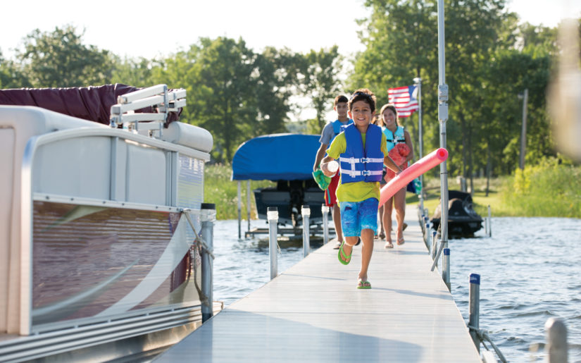 Kids wearing lifejackets running down dock towards pontoon boat.