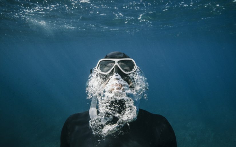 Snorkeler wearing mask and snorkel, exhaling while swimming to the surface.