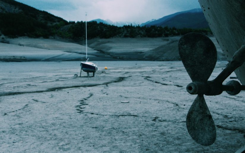 Sailboats sitting on blocks in a dried-up riverbed.