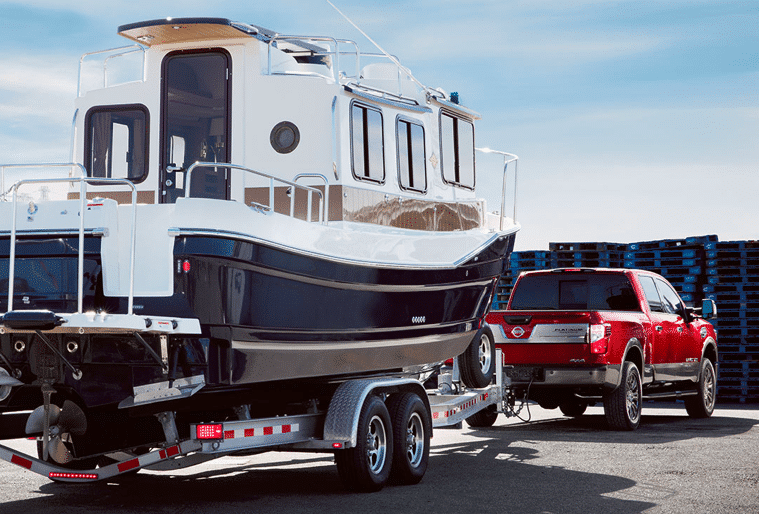 Red Nissan Titan towing massive boat, parking on a pier.