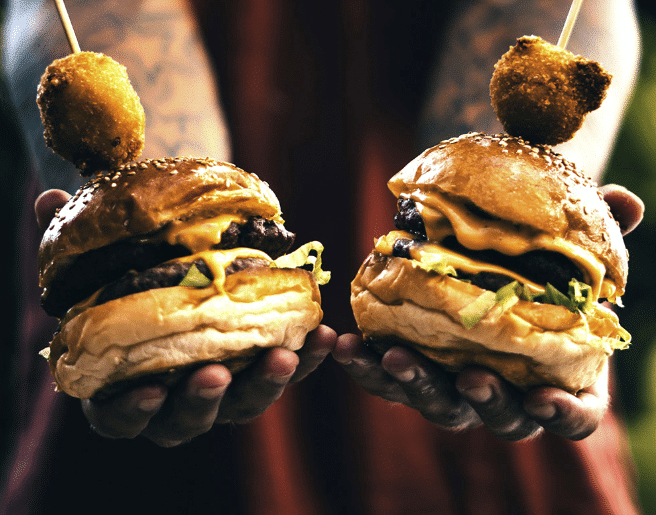 Cottager holding two recently BBQed cheeseburgers towards camera.