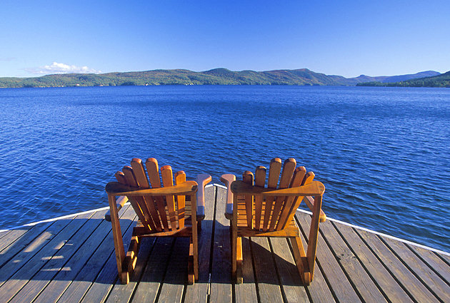 Two adirondack chairs on a dock overlooking New York lake.