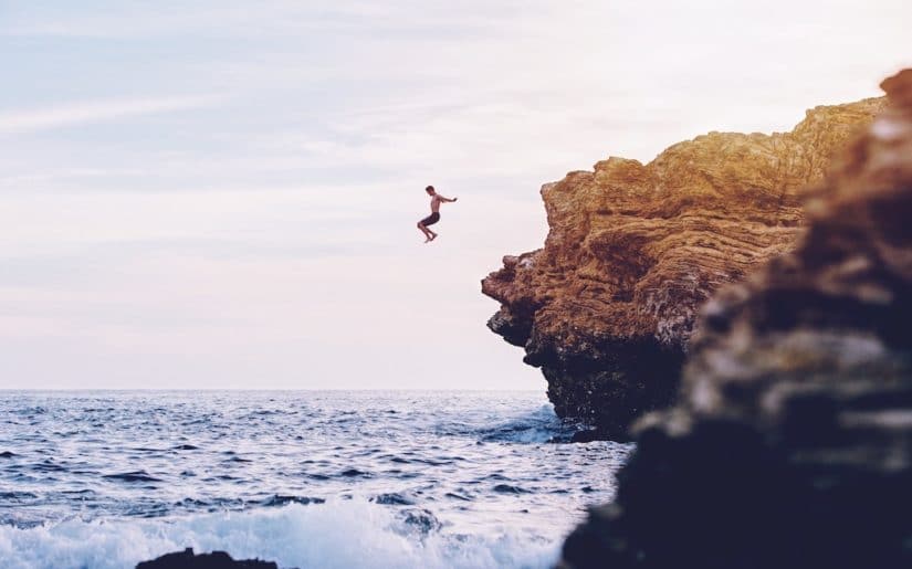 Swimmer jumping into ocean from cliffs.