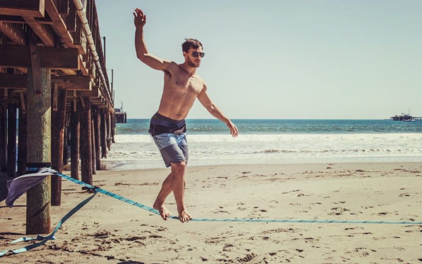 Man balancing on a slackline on beach beside a pier.