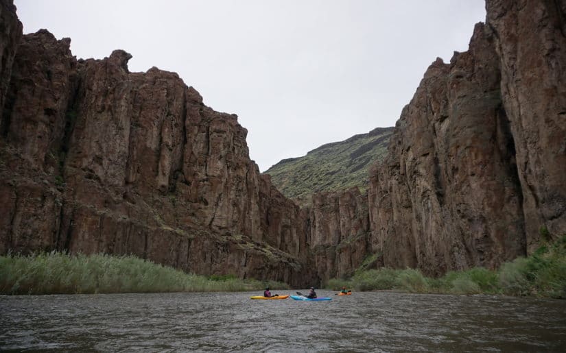 Three kayakers resting on the water below a Ecuador gorge.
